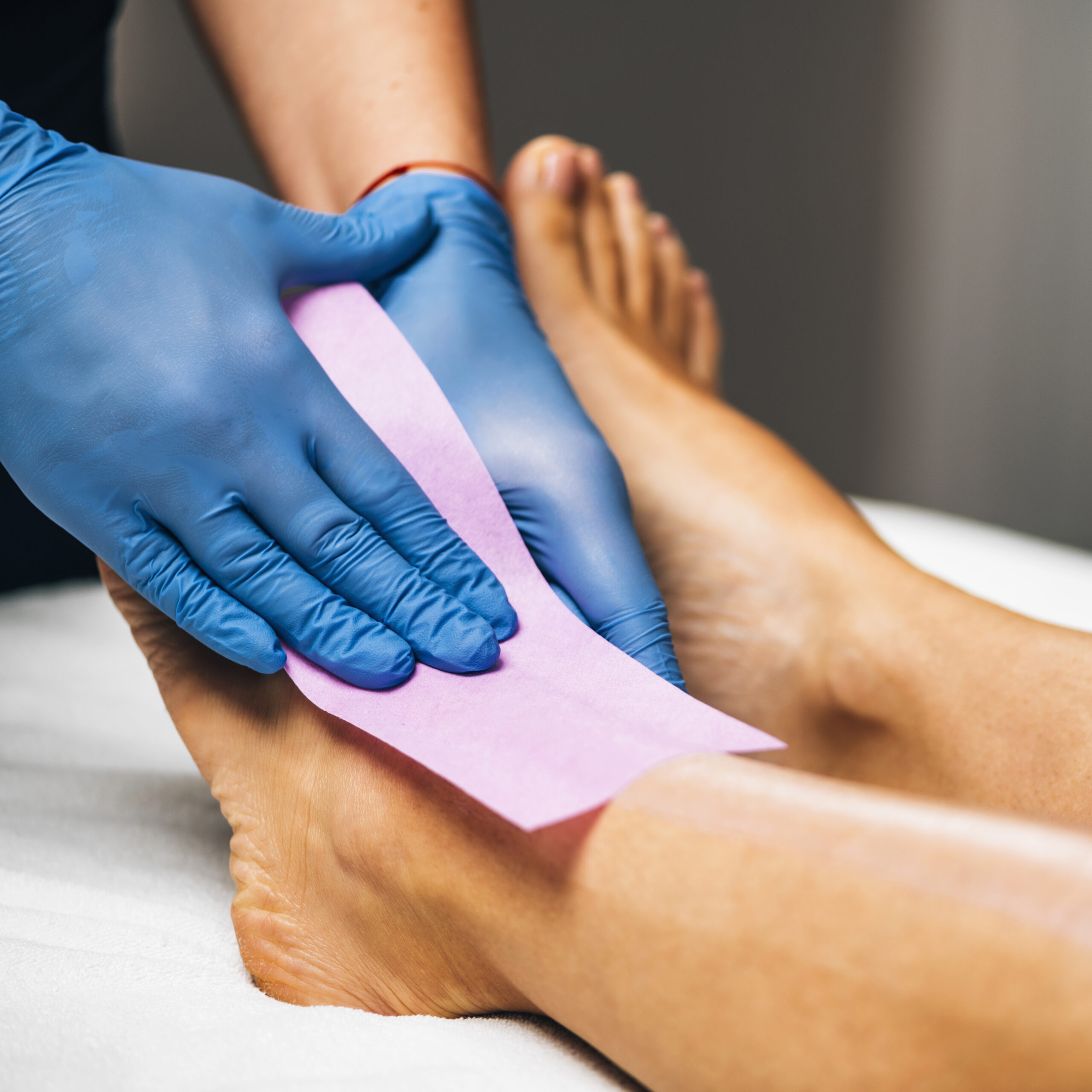 Waxing - Beautician Removing Unwanted Hair from Female Leg with Wax Strips in a Beauty Salon